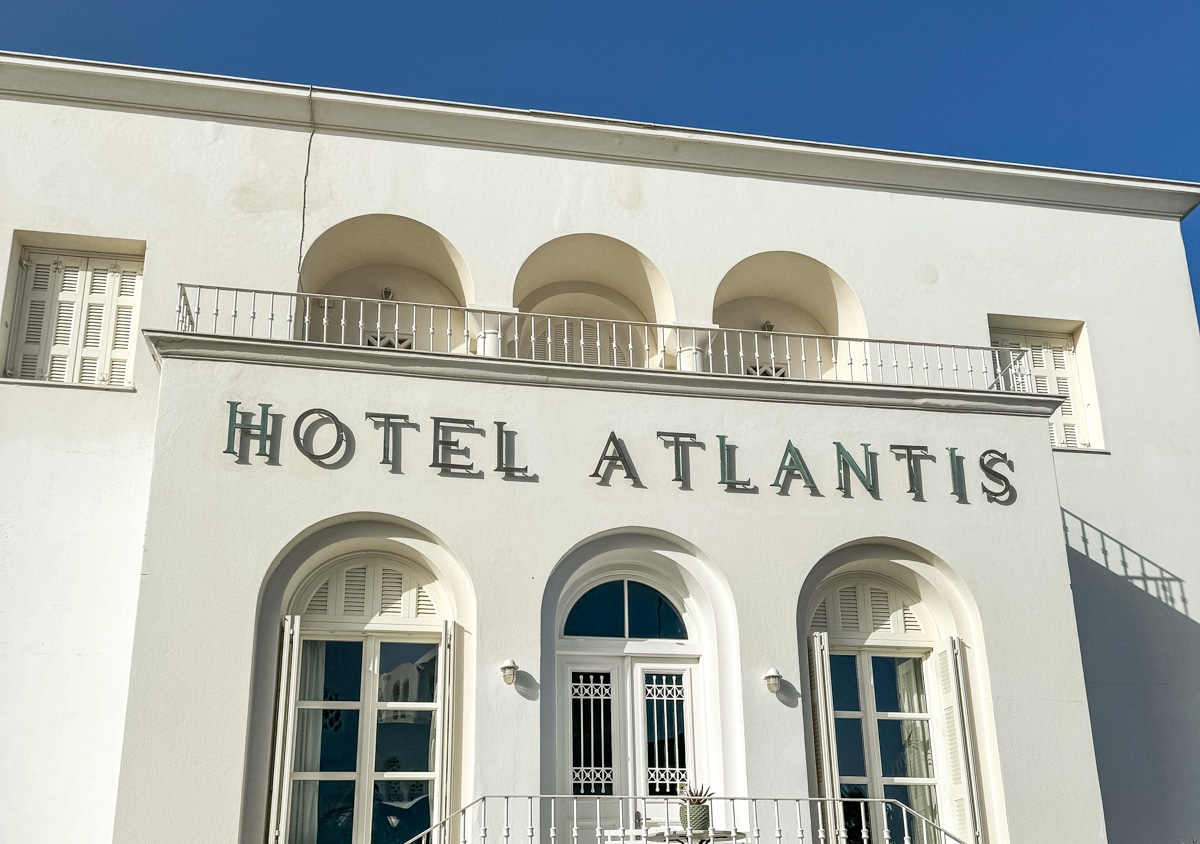 Facade of Hotel Atlantis with white arches and matching doors and windows, topped by a blue sky.