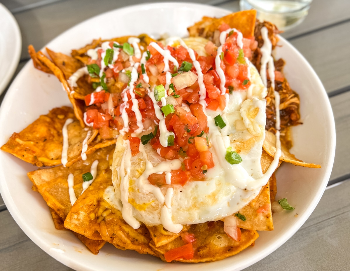 A plate of chilaquiles topped with a fried egg, salsa, chopped green onions, and drizzled with sour cream.