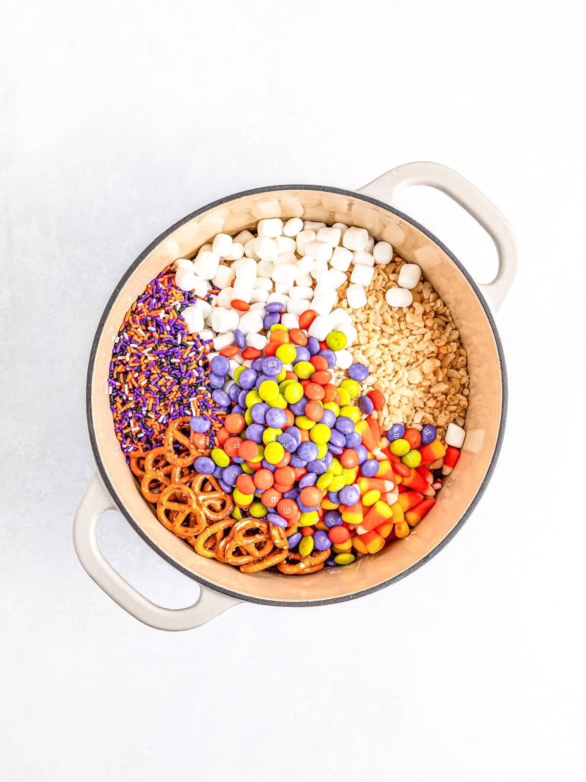 A large bowl containing Halloween Rice Krispie Treats mixed with marshmallows, crushed peanuts, colorful candies, pretzels, and purple and orange sprinkles.