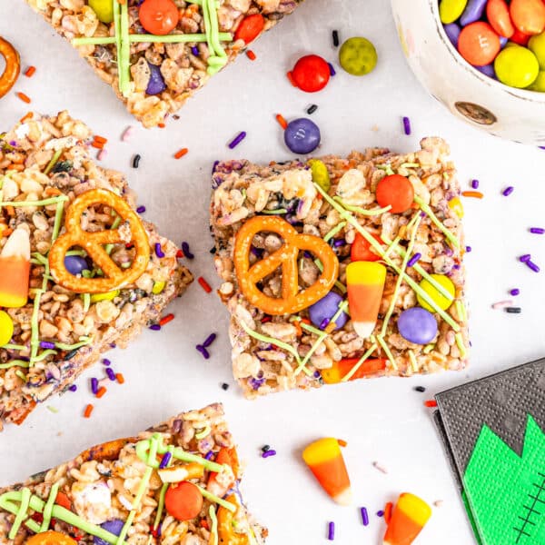 Top-down view of colorful Halloween Rice Krispie treats topped with pretzels, candy corn, and sprinkles, arranged on a white surface with scattered candies.