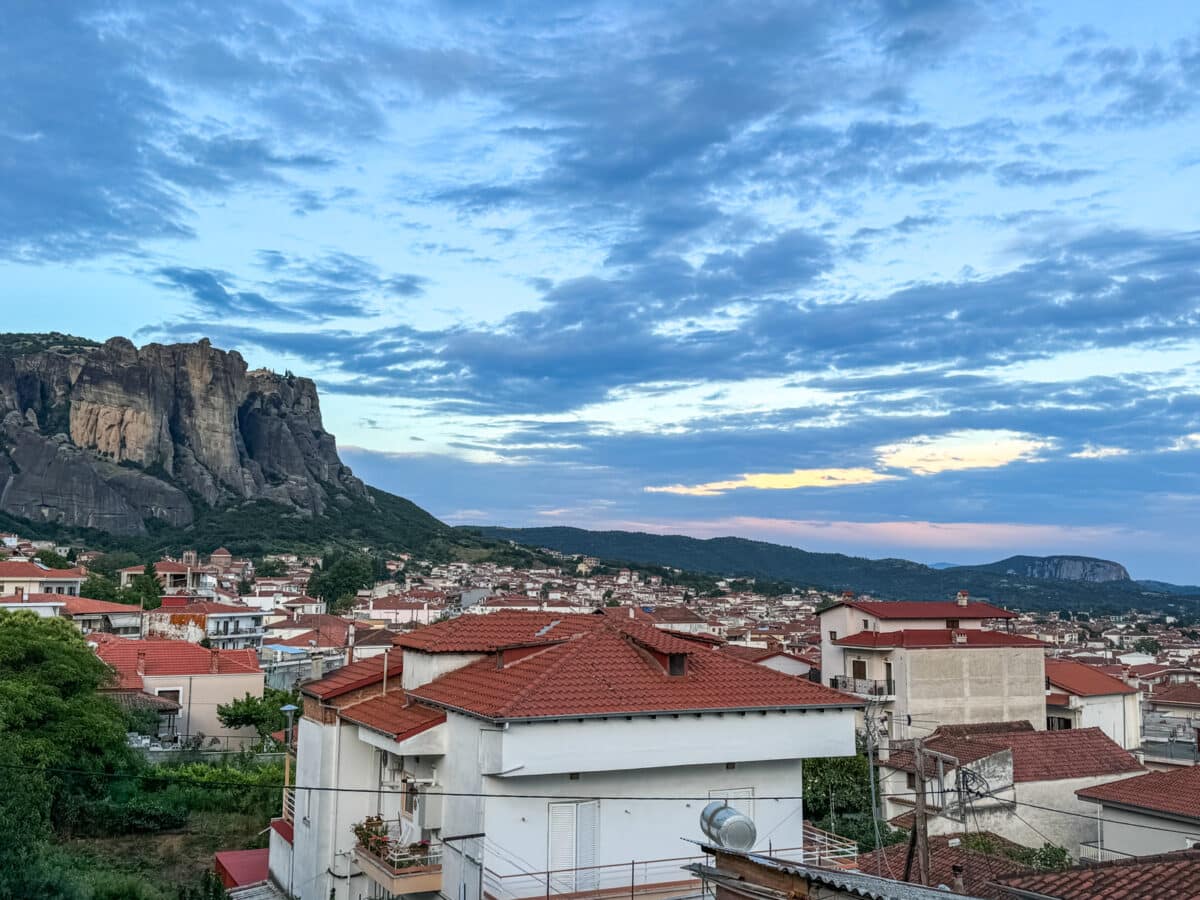 A town with white houses and red rooftops is nestled beside rocky cliffs. The sky is partly cloudy with hints of sunset light.