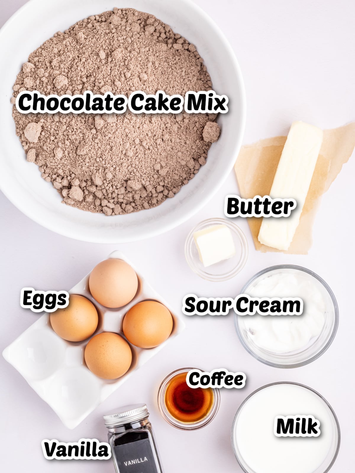 Ingredients for a chocolate cake are laid out, including chocolate cake mix, butter, eggs, sour cream, milk, vanilla extract, and coffee.