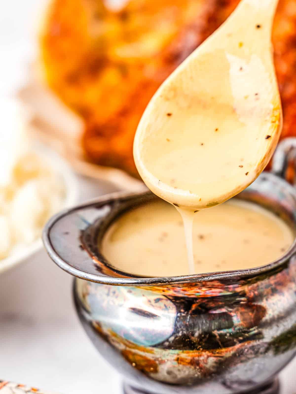 A wooden spoon drizzling creamy gravy into a small, glossy black gravy boat.