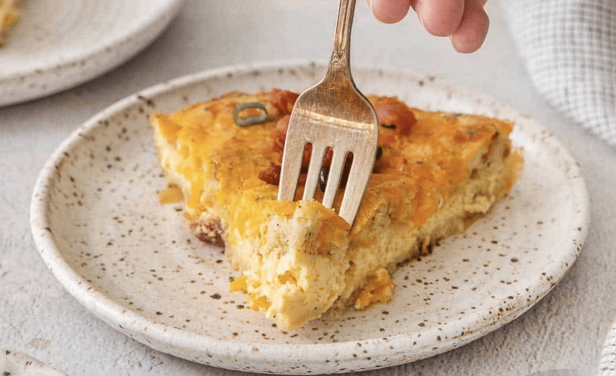 A fork cutting into a slice of quiche on a speckled plate.