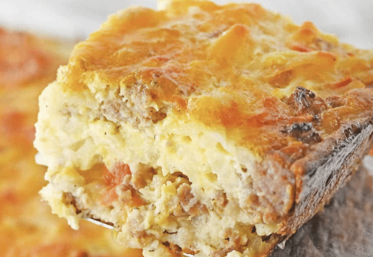 A close-up of a slice of savory breakfast casserole with visible layers of meat, egg, and melted cheese.