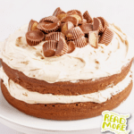 A decadent two-layer peanut butter cup cake topped with creamy peanut butter frosting and adorned with mini peanut butter cups, elegantly presented on a white cake stand.