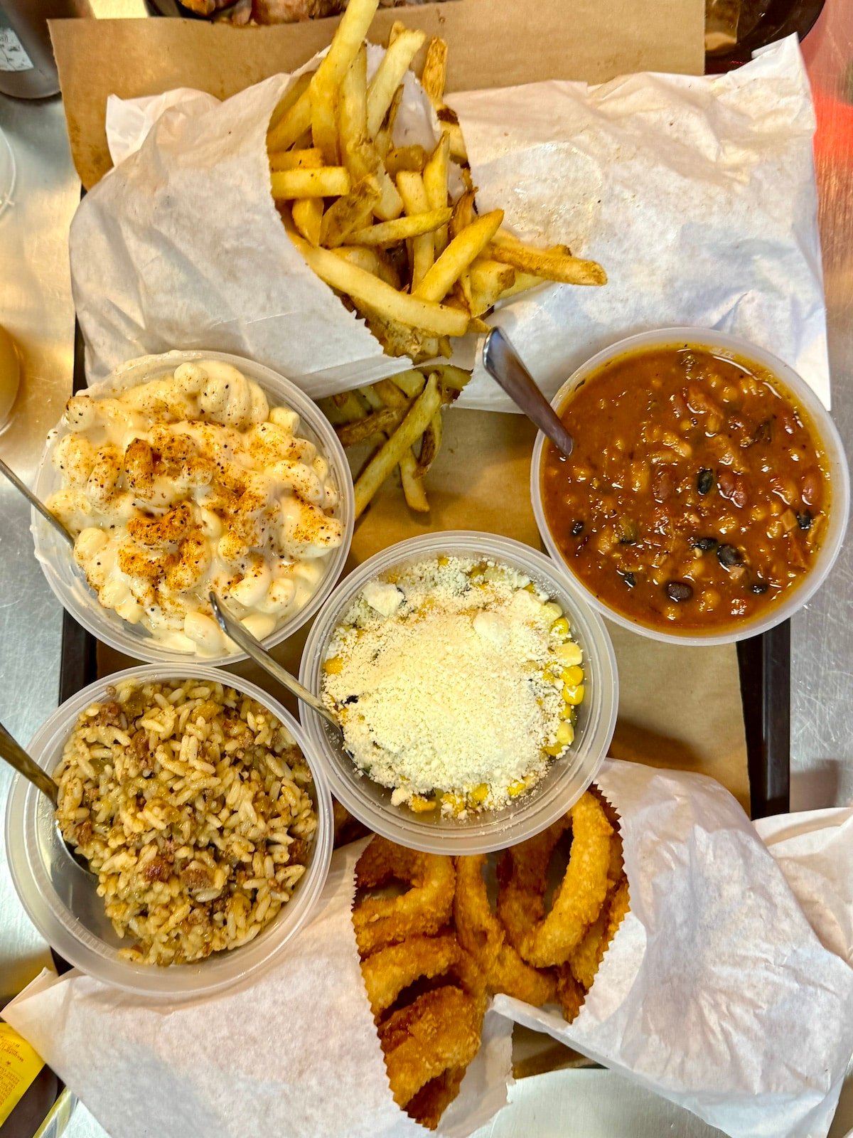 Tray with fries, onion rings, mac and cheese, chili beans, rice, and corn topped with cheese.