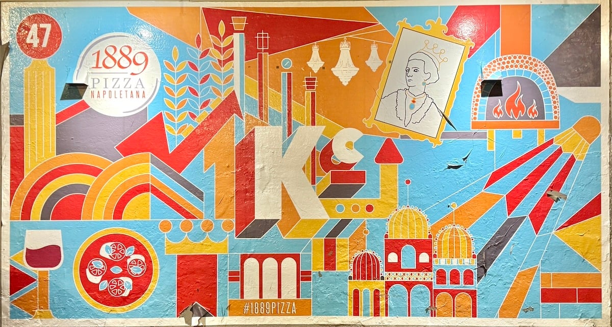 Colorful mural featuring pizza elements, a crown, bottles, and architectural motifs, with "1889 Pizza Napolitana" and "1K" prominently displayed.