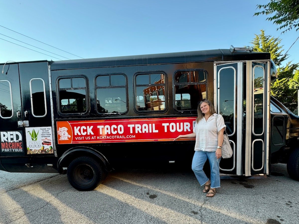 A person stands next to a black bus labeled "KCK Taco Trail Tour.