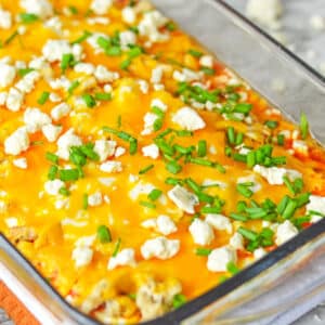 A glass baking dish with baked casserole topped with melted cheese, crumbled white cheese, and chopped green onions.