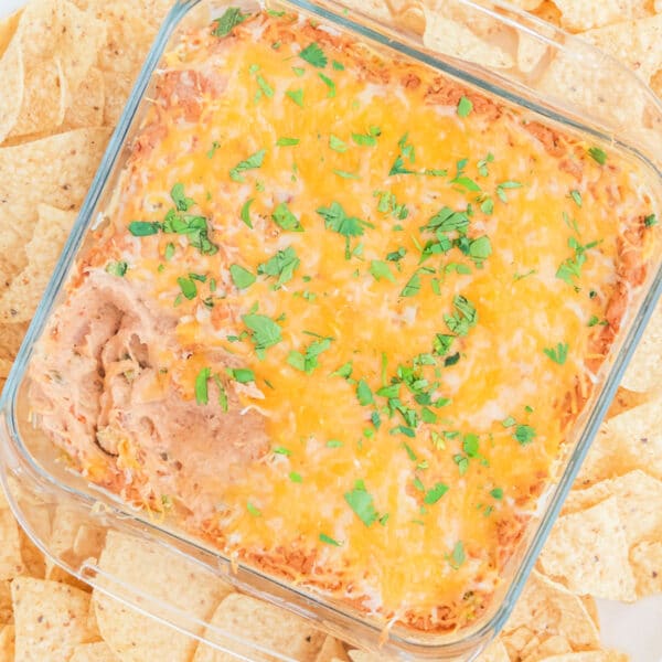 Glass dish with baked bean dip topped with melted cheese and chopped herbs, surrounded by tortilla chips.