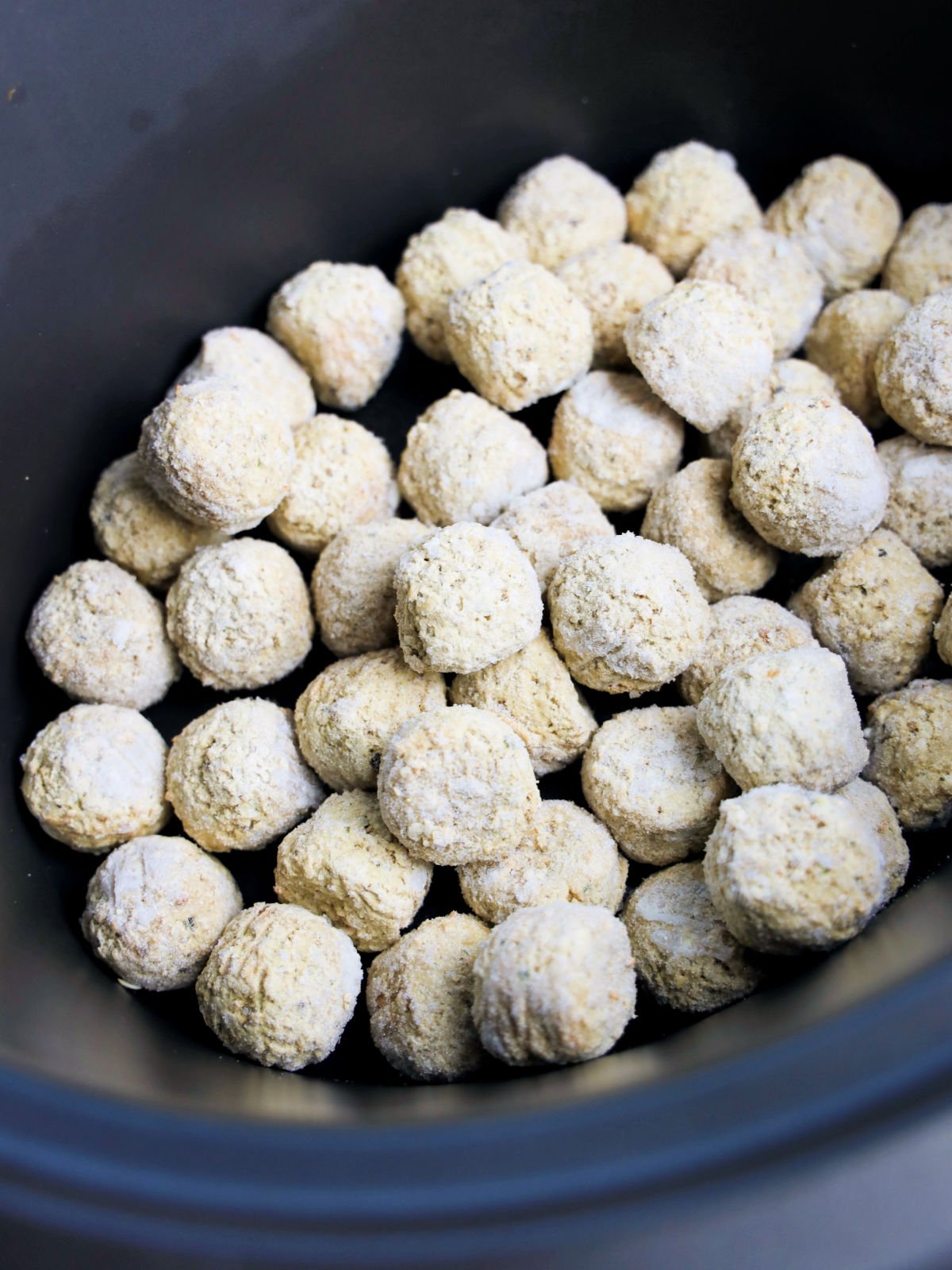 A black bowl filled with numerous small, round, evenly coated dough balls.