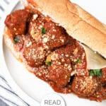 Meatball sub sandwich with tomato sauce and Parmesan cheese on a white plate. Text overlay reads "READ MORE MEATBALL SUBS.