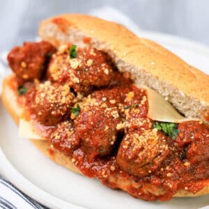 A meatball sub on a plate, topped with tomato sauce, grated cheese, and herbs, in a crusty baguette.