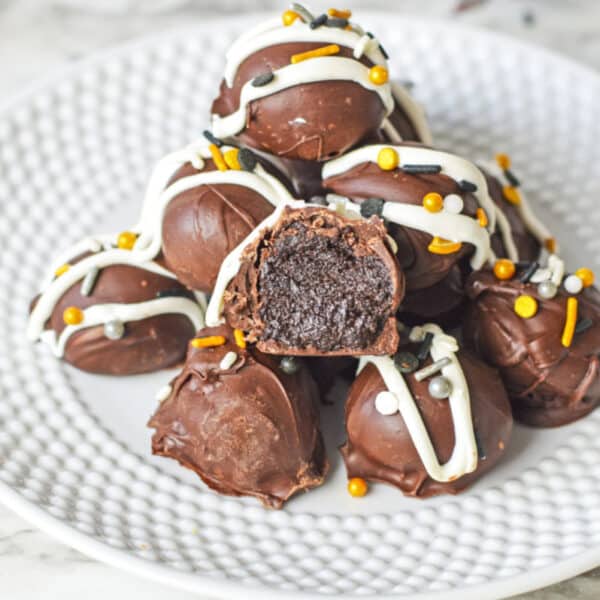 A plate of chocolate truffles stacked in a pyramid, with one truffle cut open to show the inside. Decorated with white icing and sprinkles.