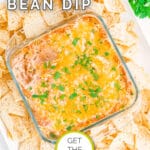 Glass dish of refried bean dip topped with melted cheese and green onions, surrounded by tortilla chips, on a white background.