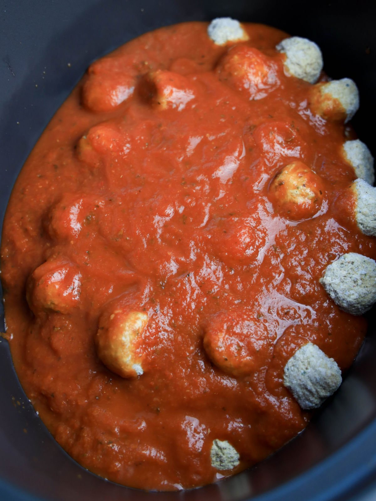 Meatballs partially submerged in red tomato sauce, placed inside a dark slow cooker pot.