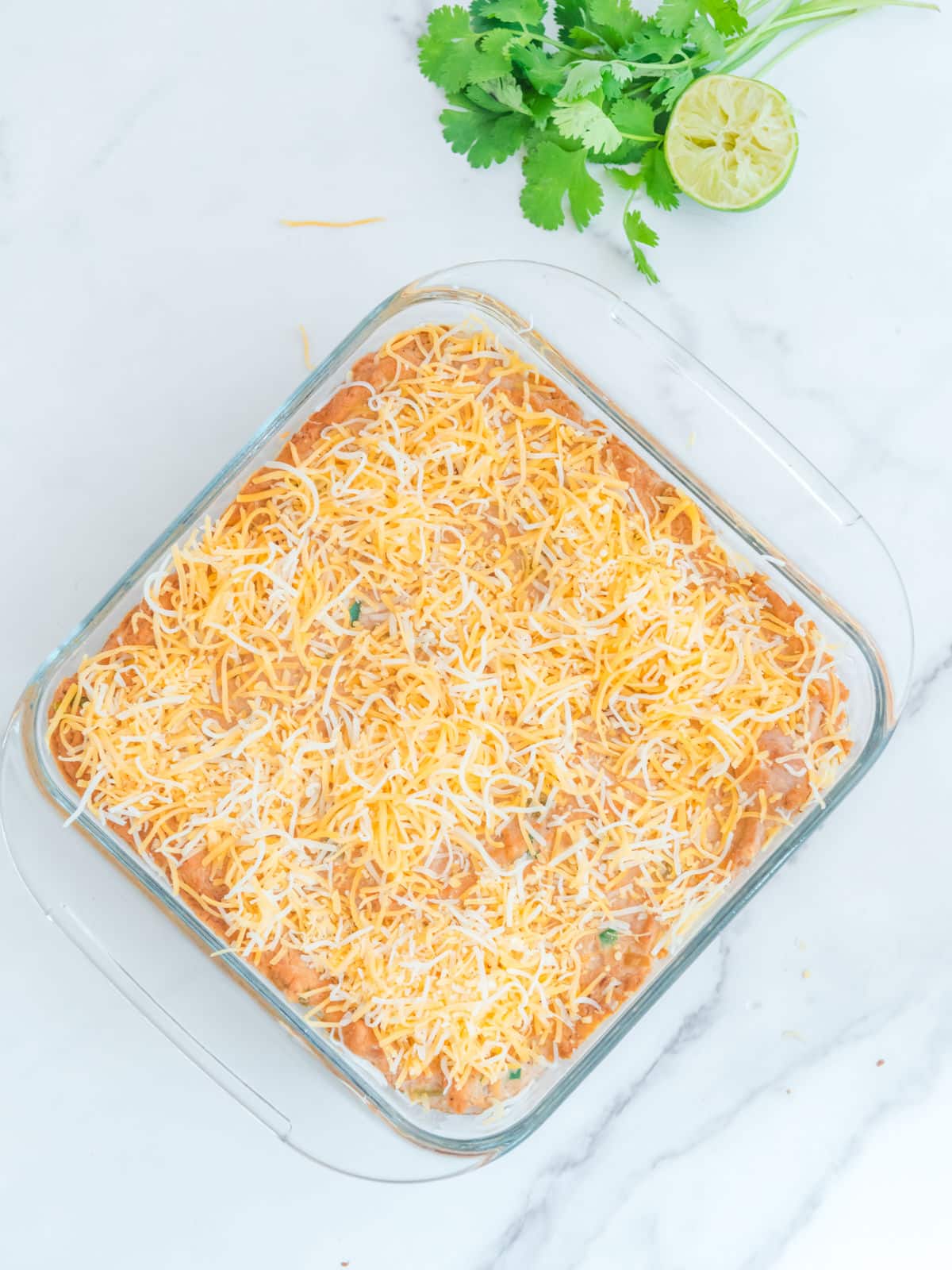 Glass dish of shredded cheese on top of a baked dish, garnished with cilantro and lime on the side.