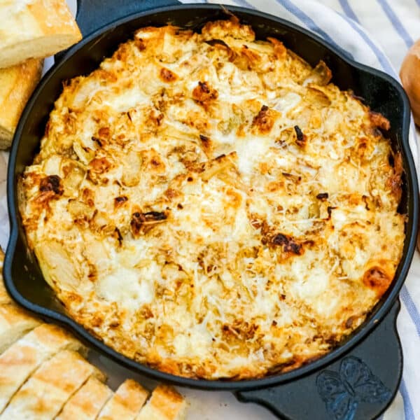 Cheesy baked dip in a cast iron skillet, surrounded by slices of bread on a striped cloth.