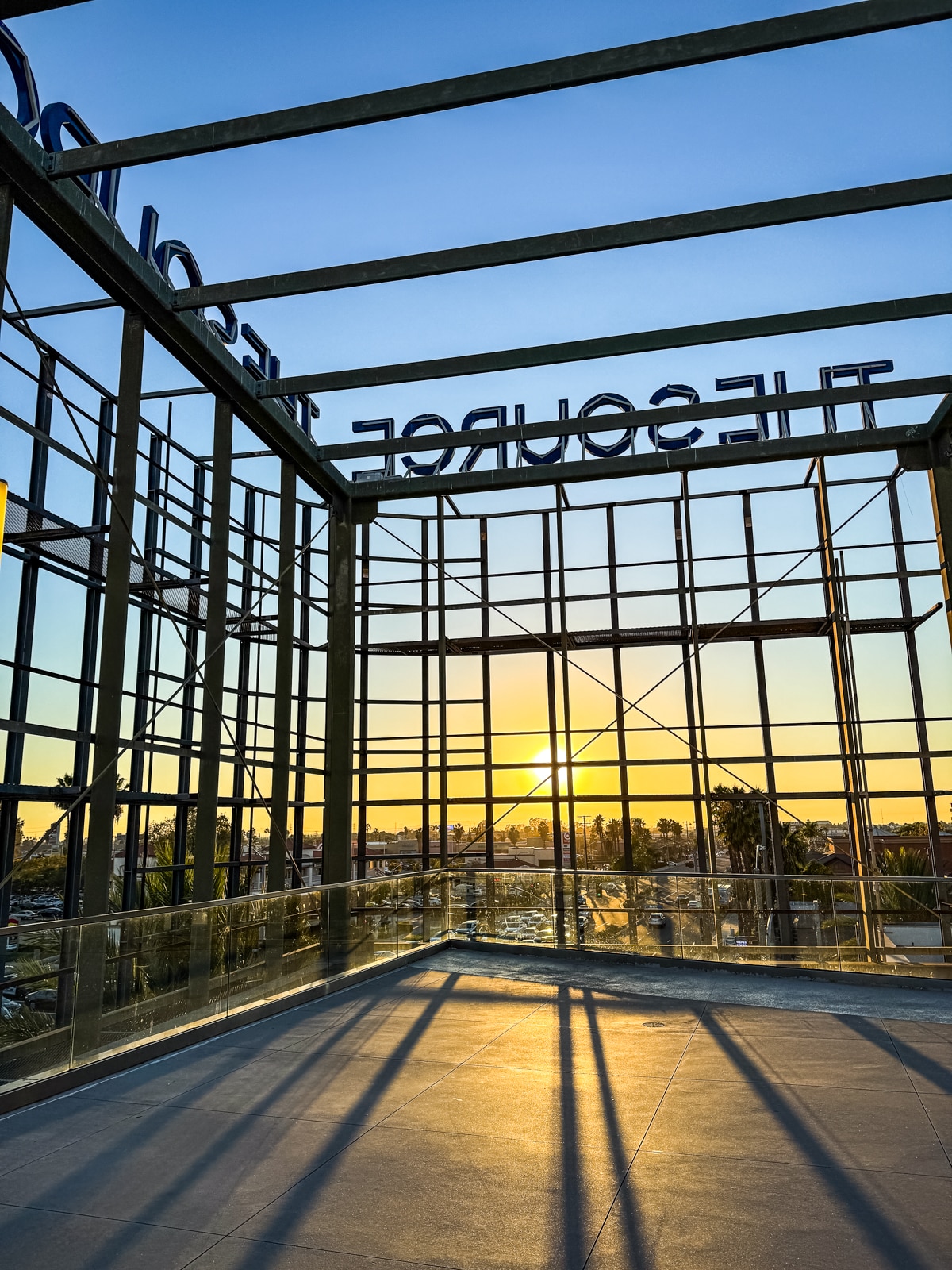 Metal framework structure on a rooftop at sunset, with the sun low on the horizon and cityscape visible through the grid.