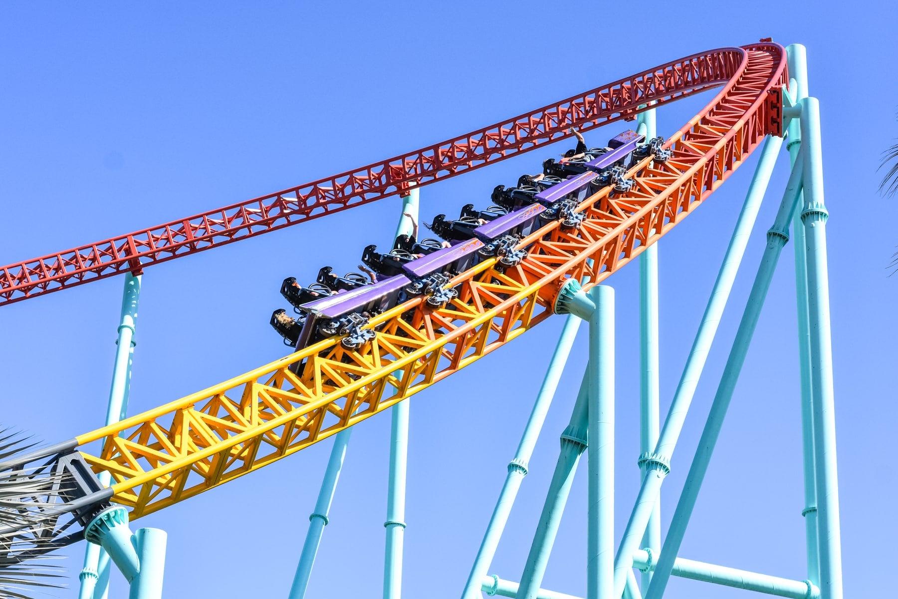 A brightly colored roller coaster with empty cars is ascending a steep track against a clear blue sky.
