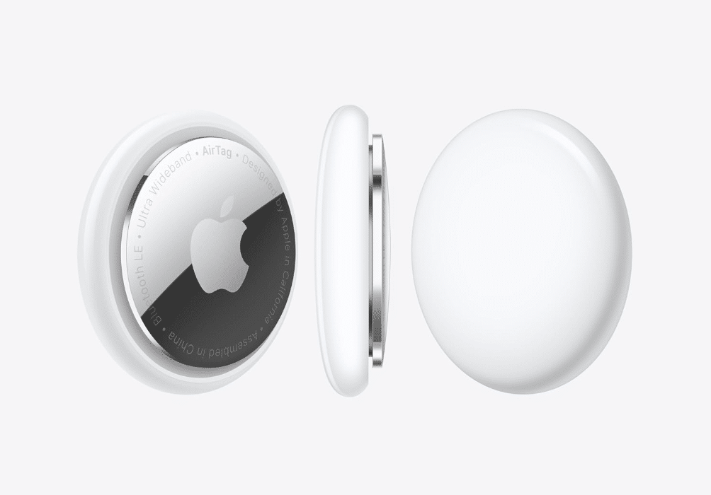 Three Apple AirTag devices shown; one displays the Apple logo and product text, another shows a side profile, and the third displays the smooth, plain white side.