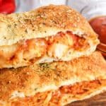 Two pieces of Chicken Parm Stromboli stuffed bread with melted cheese and tomato sauce, topped with herbs and grated cheese, served alongside a bowl of marinara sauce.