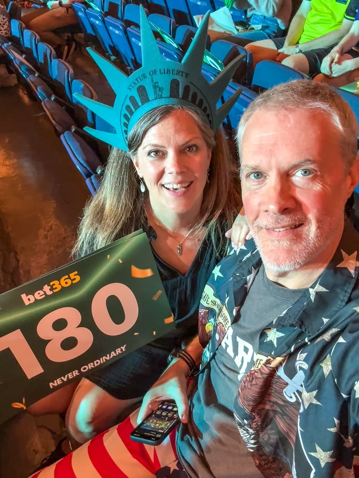 A woman wearing a Statue of Liberty crown and a man in a star-spangled shirt hold a "180" sign at a crowded indoor event.