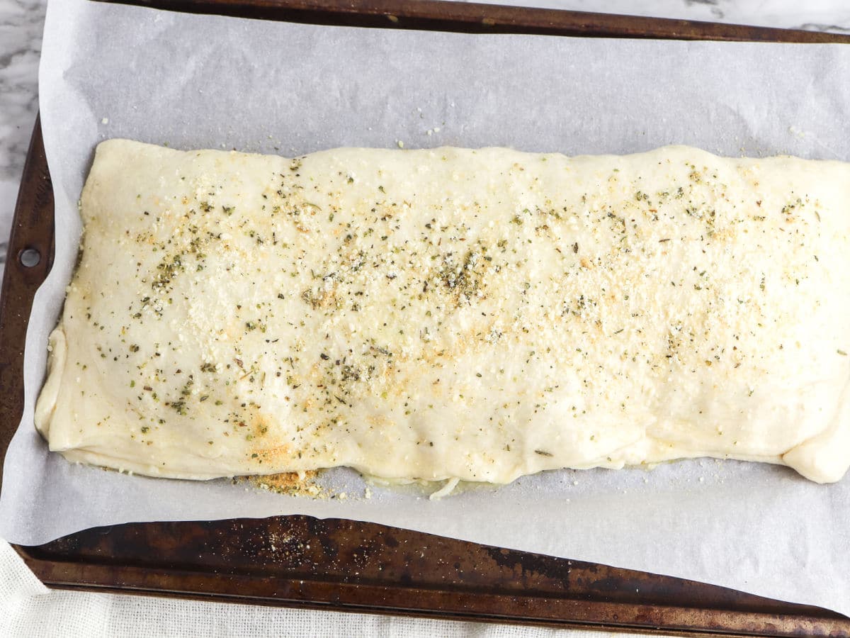 Unbaked, seasoned dough stuffed with Chicken Parm Stromboli filling on a parchment-lined baking sheet, ready to be cooked.