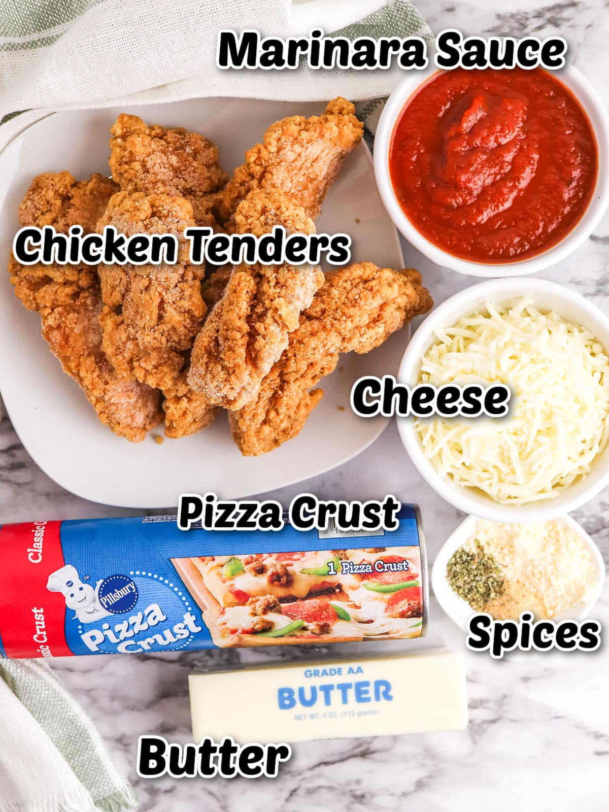 A plate with ingredients for Chicken Parm Stromboli: chicken tenders, a bowl of marinara sauce, shredded cheese, canned pizza crust, butter, and small piles of spices on a marble surface.