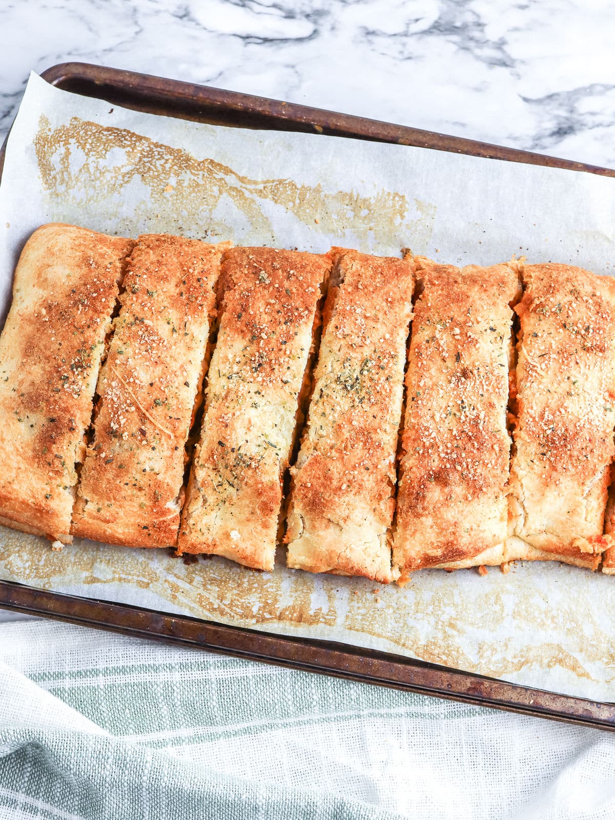 A rectangular loaf of Chicken Parm Stromboli, sliced into six pieces, sits on a parchment-lined baking sheet. The bread has a golden, seasoned crust.