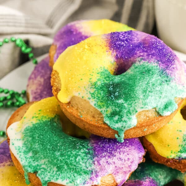 A plate of donuts decorated with white icing and yellow, green, and purple sugar, resembling Mardi Gras colors.