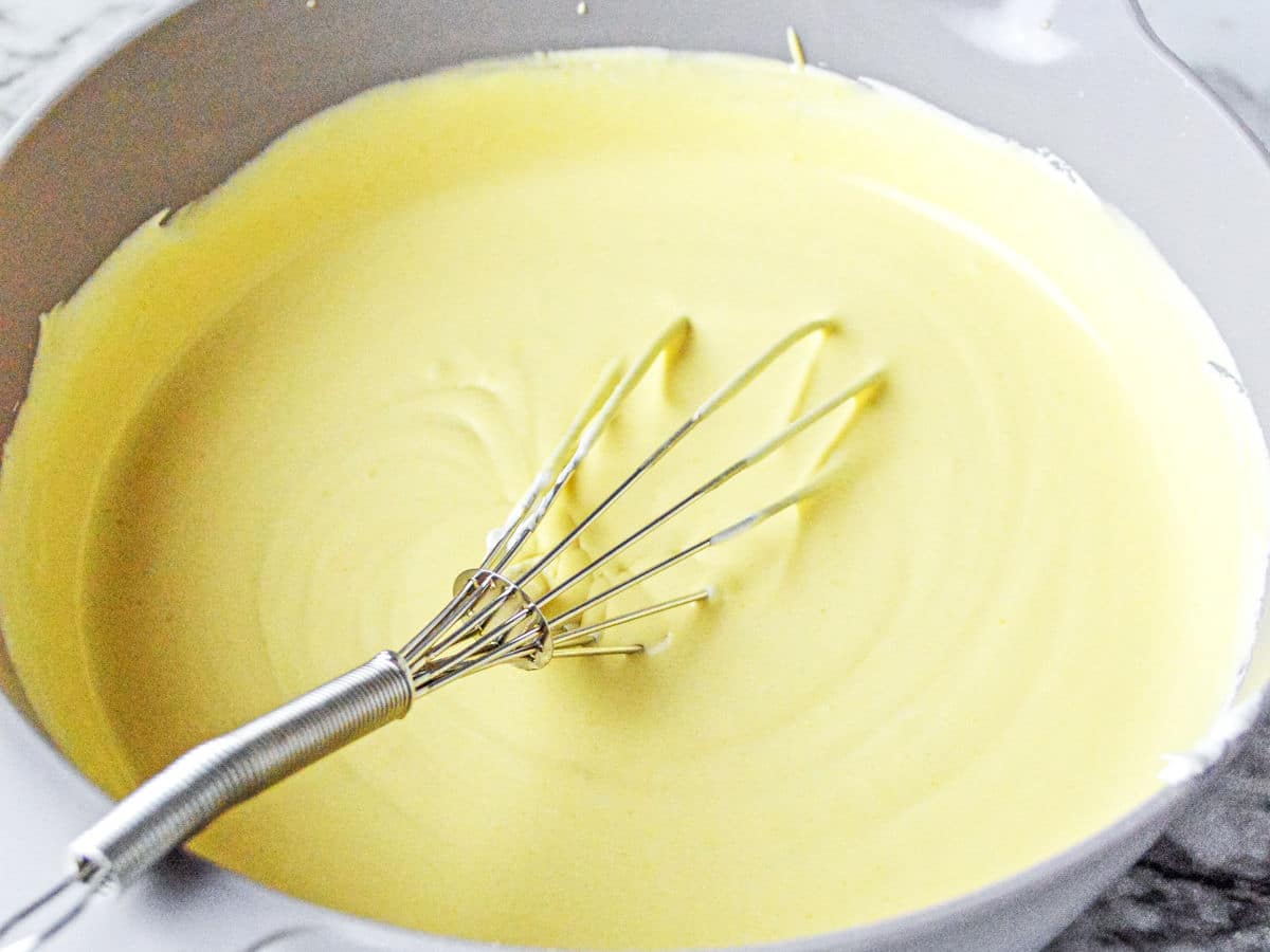 A metal whisk rests in a bowl filled with smooth, pale yellow batter.
