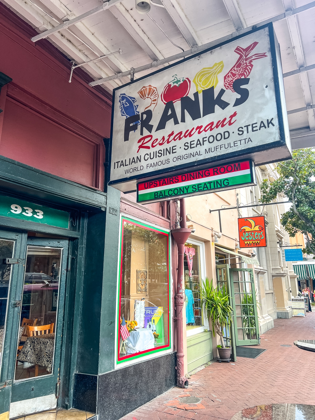 Street view of Franks Restaurant with a large sign advertising Italian cuisine, seafood, steak, and muffuletta, located next to a shop with a green door numbered 933.