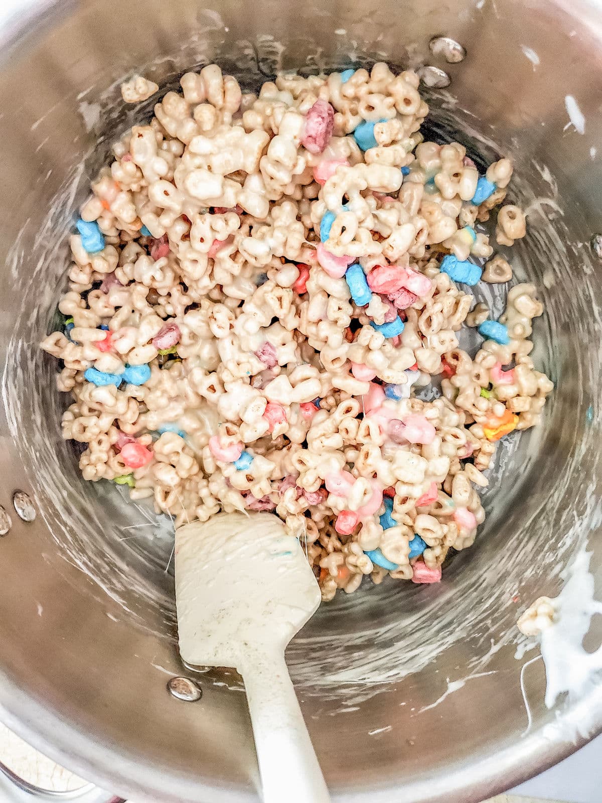 A pot filled with a mixture of cereal, colorful marshmallows, and melted marshmallow, with a spatula partially covered in the mixture.