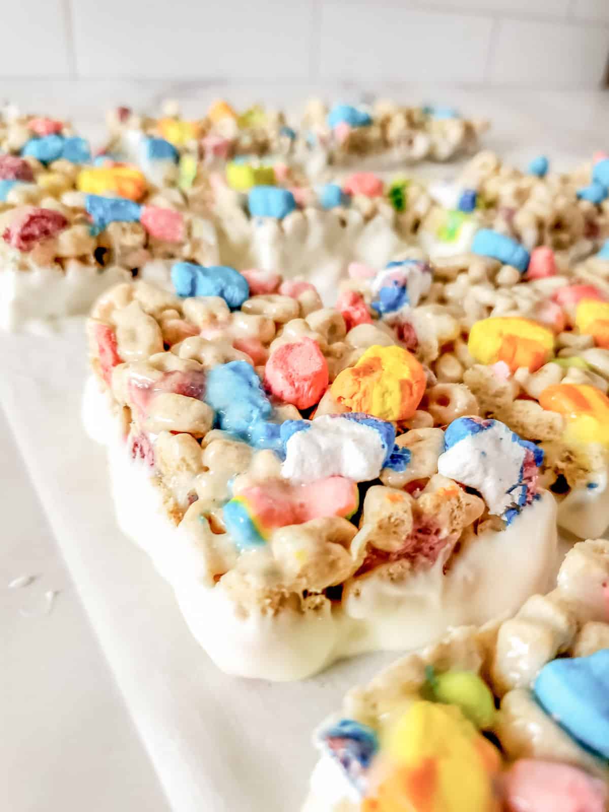 Close-up of cereal bars made with colorful marshmallow cereal and what appears to be a white coating, arranged on a white surface.