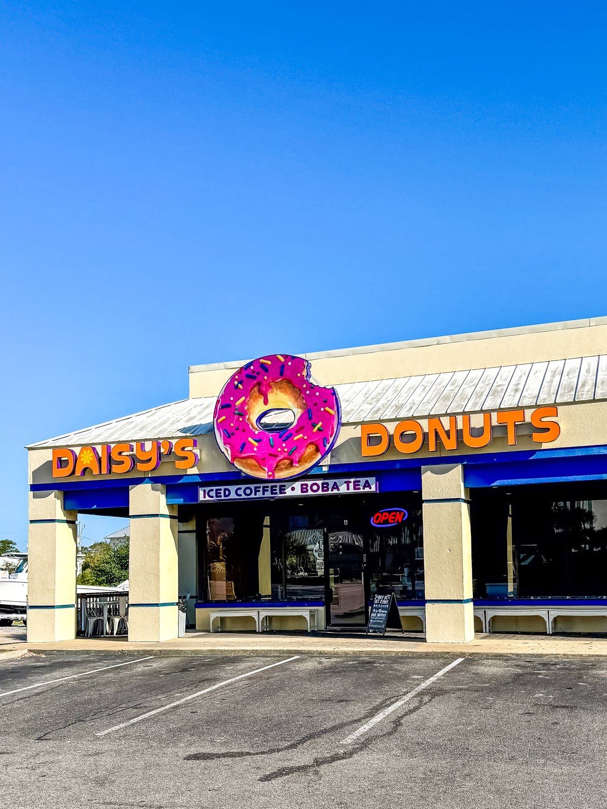 A donut shop called Daisy's Donuts with a large pink donut sign above the entrance and an open sign in the window.