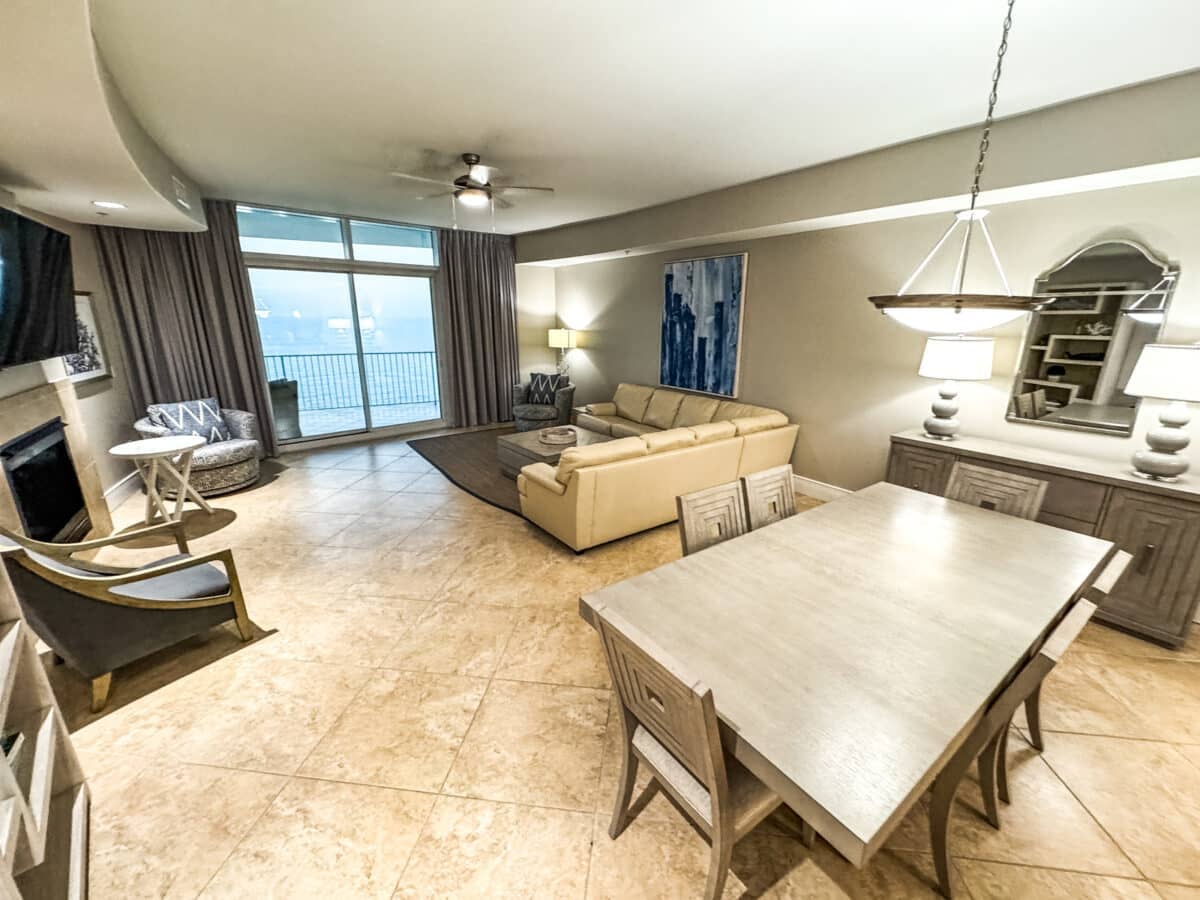 Spacious living and dining area with tile flooring, beige sofa, dining table with six chairs, large windows, and balcony view.