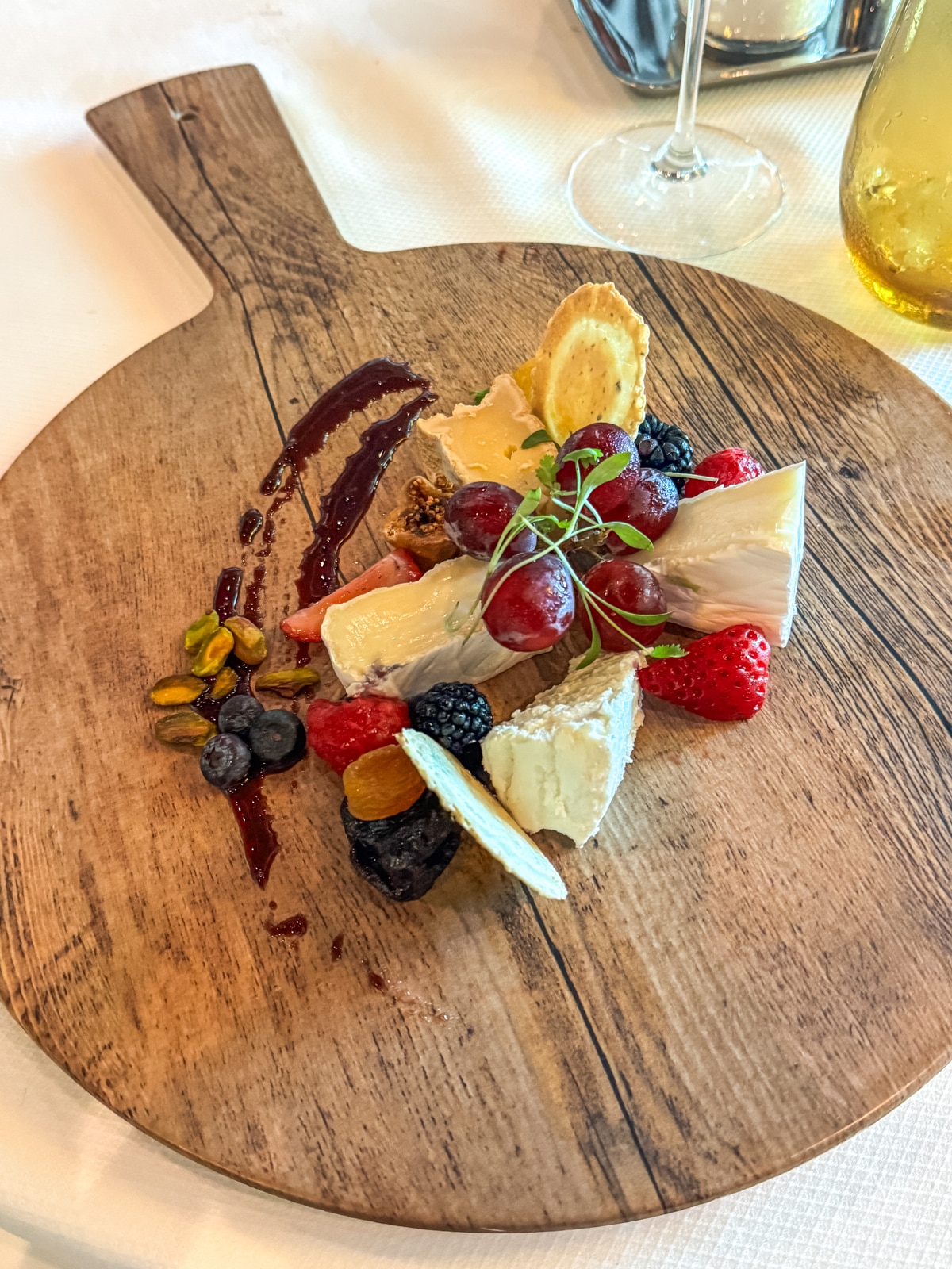 A wooden serving board with assorted cheeses, berries, grapes, nuts, crackers, and a swirl of berry sauce, accompanied by a wine glass—perfect for sharing on a Holland America with teens cruise experience.