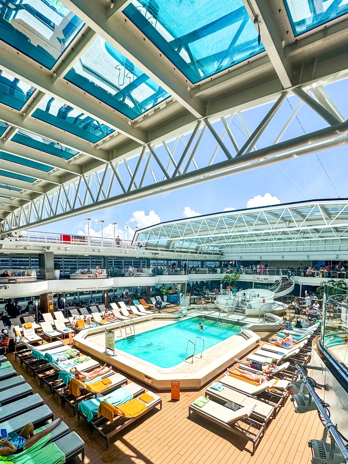 A cruise ship pool deck with lounge chairs, a swimming pool, and a retractable glass roof overhead—perfect for enjoying sunny days on Holland America with teens.
