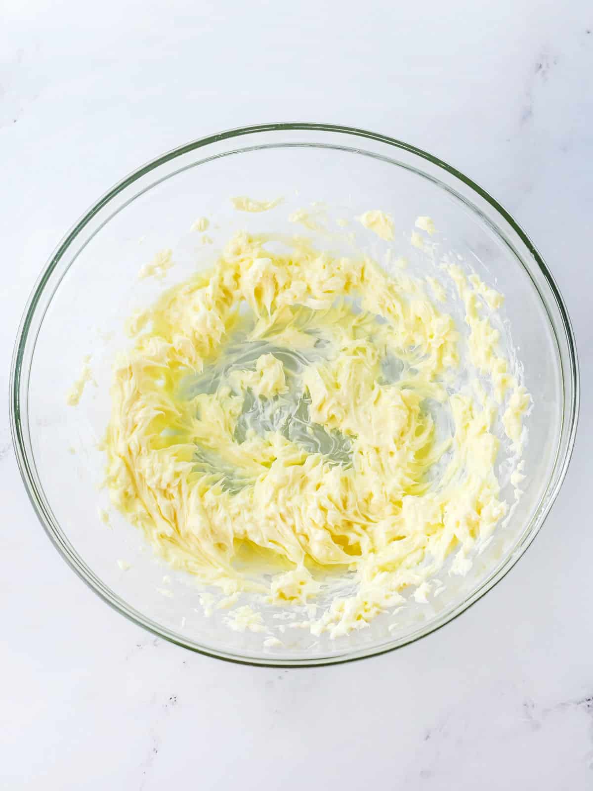 A glass bowl containing whipped or creamed butter on a white surface.