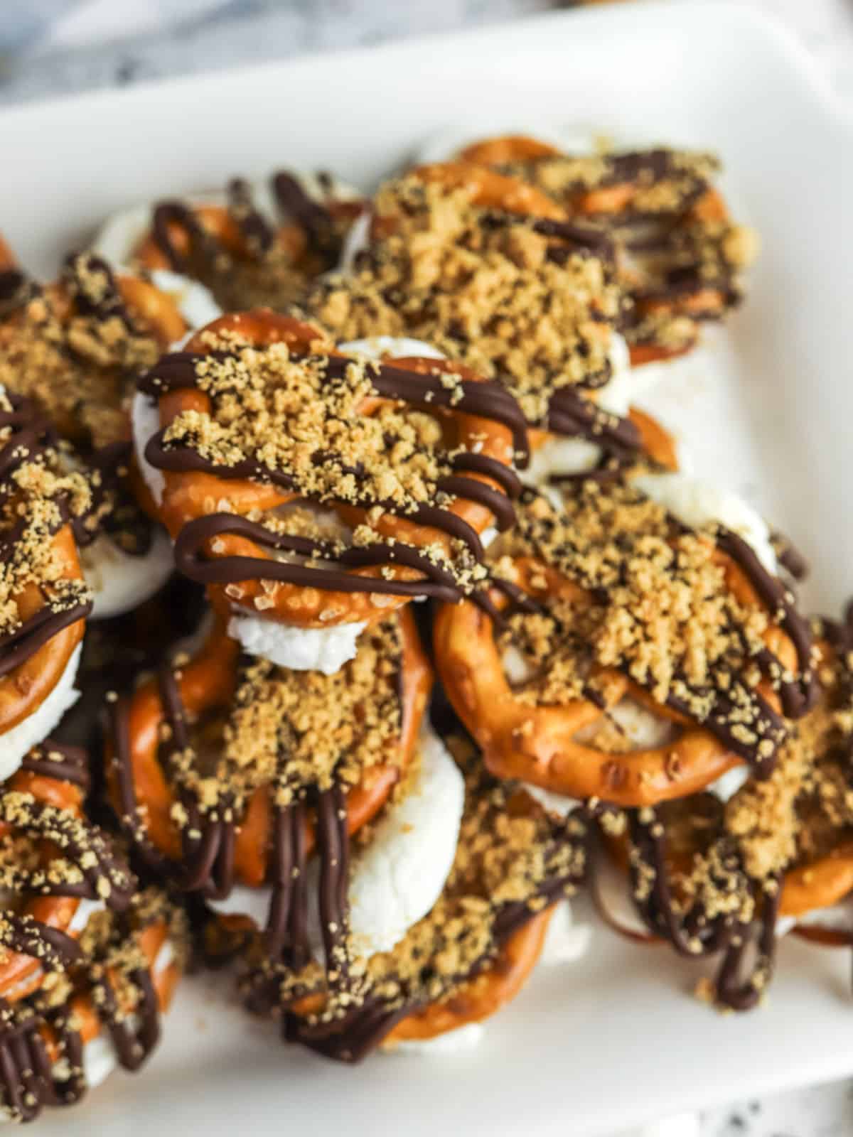 A plate of pretzel snacks topped with marshmallows, chocolate drizzle, and crushed graham crackers.