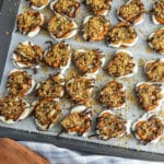 A baking tray lined with parchment paper holds clusters of pretzels topped with white coating, chocolate drizzle, and crumbly topping.