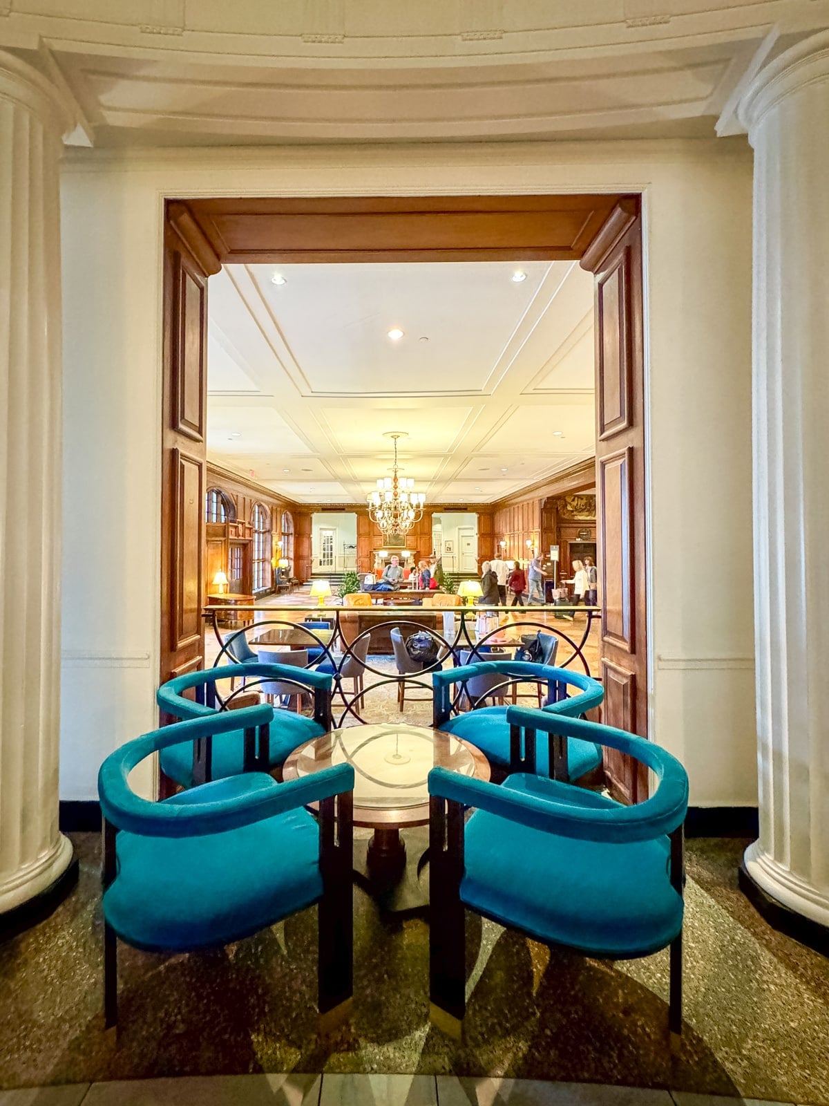 Two blue chairs and a small table sit before an open doorway, inviting you into an elegant lounge with a chandelier&mdash;one of the relaxing Things to Do in Roanoke VA for those seeking comfort and style.