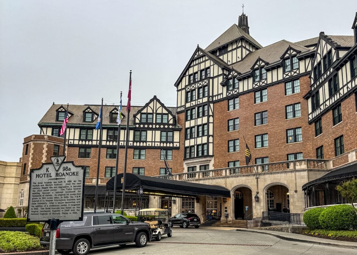 A historic multi-story Tudor-style hotel with flags at the entrance, a vintage car, and a sign reading "Hotel Roanoke" in the foreground&mdash;an iconic landmark among the top things to do in Roanoke VA.