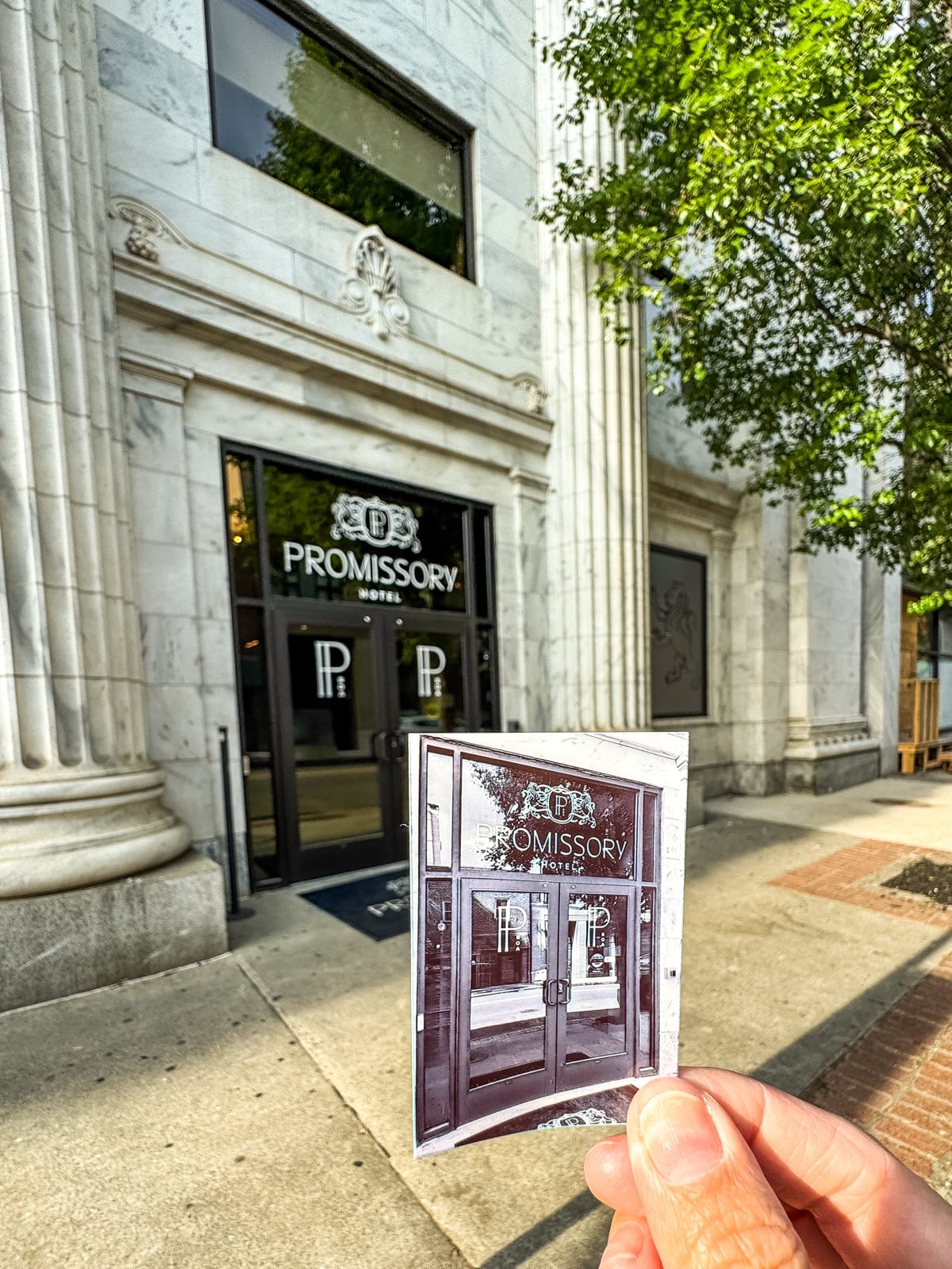 A hand holds a vintage photo of the Promissory Hotel entrance, aligning it with the current building fa&ccedil;ade on a sunny day&mdash;one of many unique things to do in Roanoke VA for history enthusiasts.