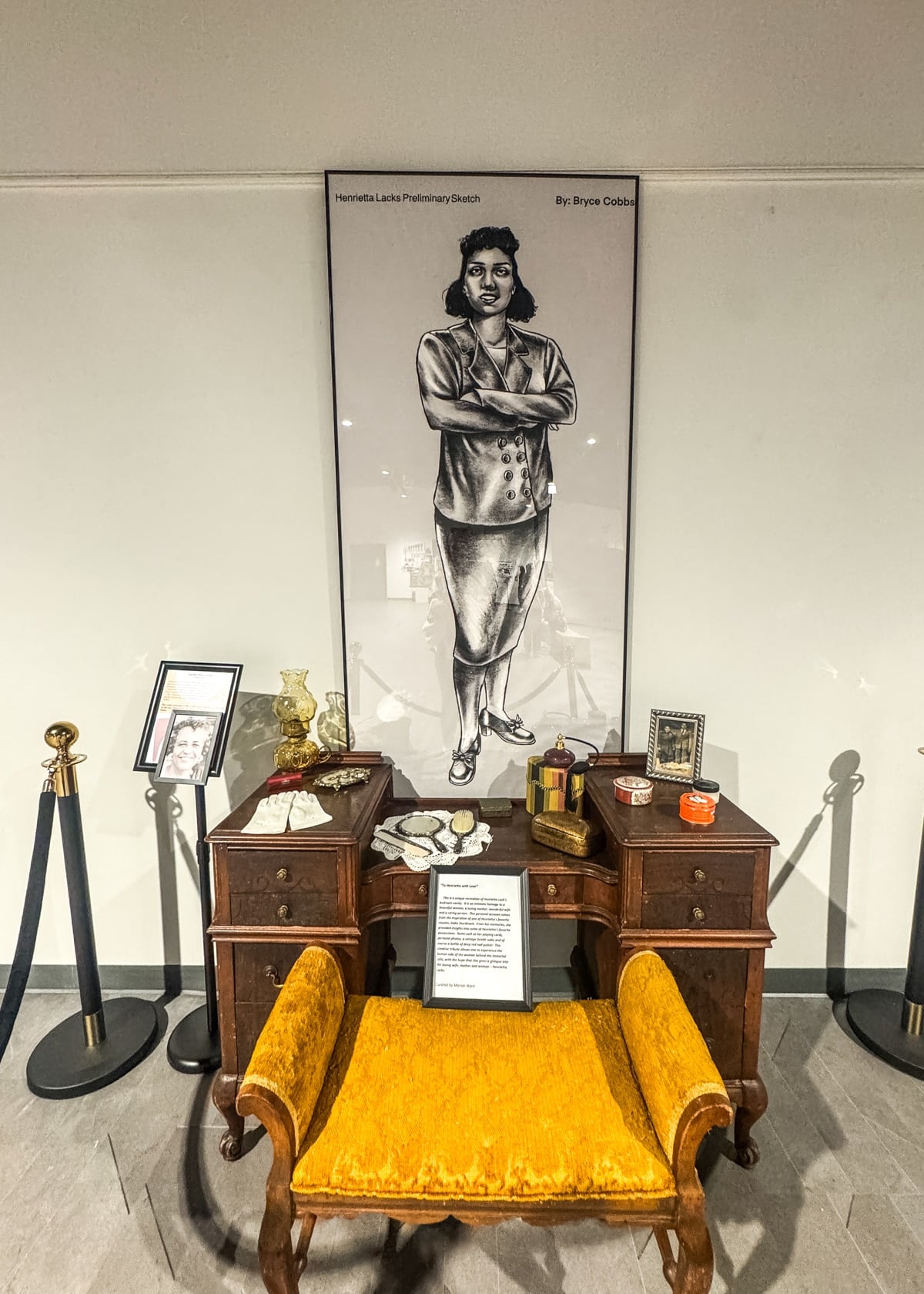 A framed portrait of a woman stands above an antique desk with various items, including framed photos, books, and a yellow upholstered chair at the Harrison Museum &mdash;inviting you to discover unique things to do in Roanoke VA.