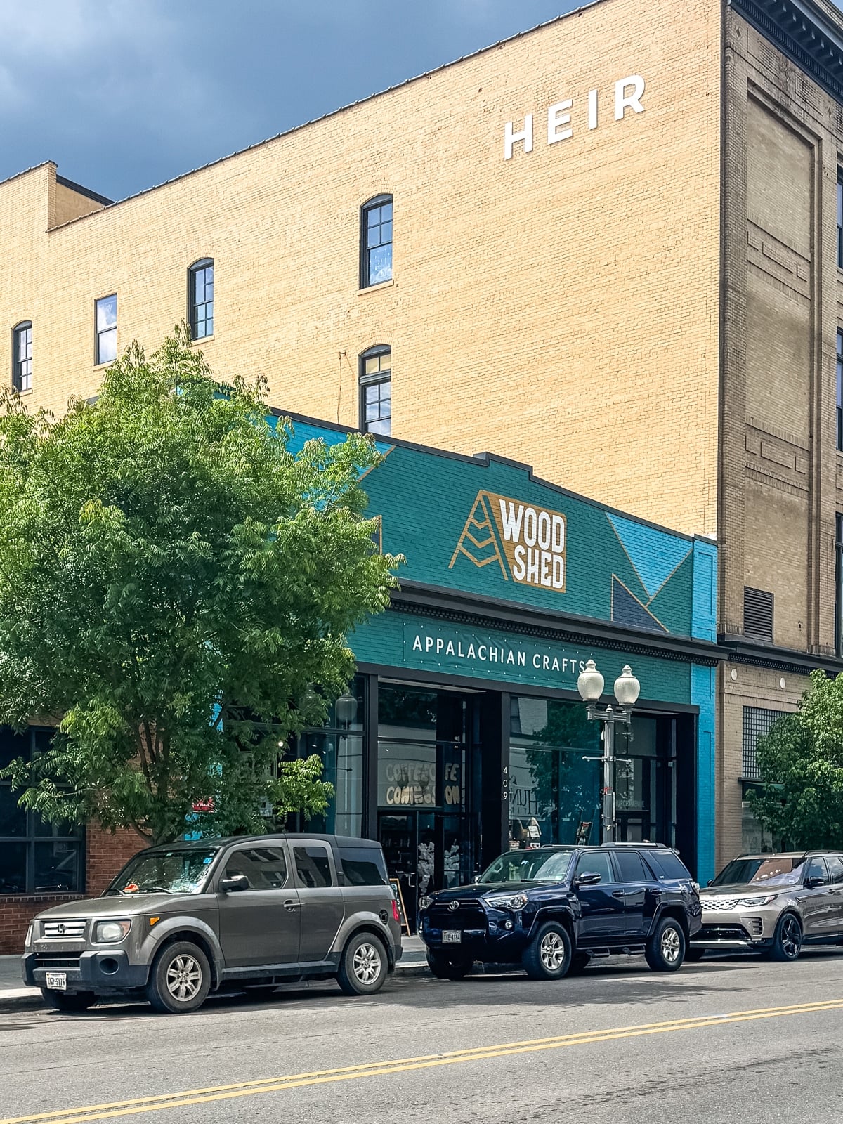 Street view of a brick building with signs reading "WOOD SHED" and "APPALACHIAN CRAFTS"&mdash;a must-see spot for those exploring Things to Do in Roanoke VA; cars line the street outside this charming storefront.