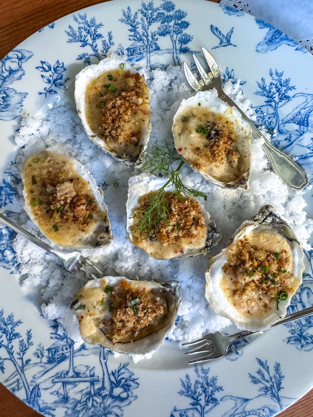 Six baked oysters topped with breadcrumbs and herbs are served on a bed of coarse salt, with three small forks&mdash;an elegant choice among the Things to Do in Roanoke VA for food lovers.