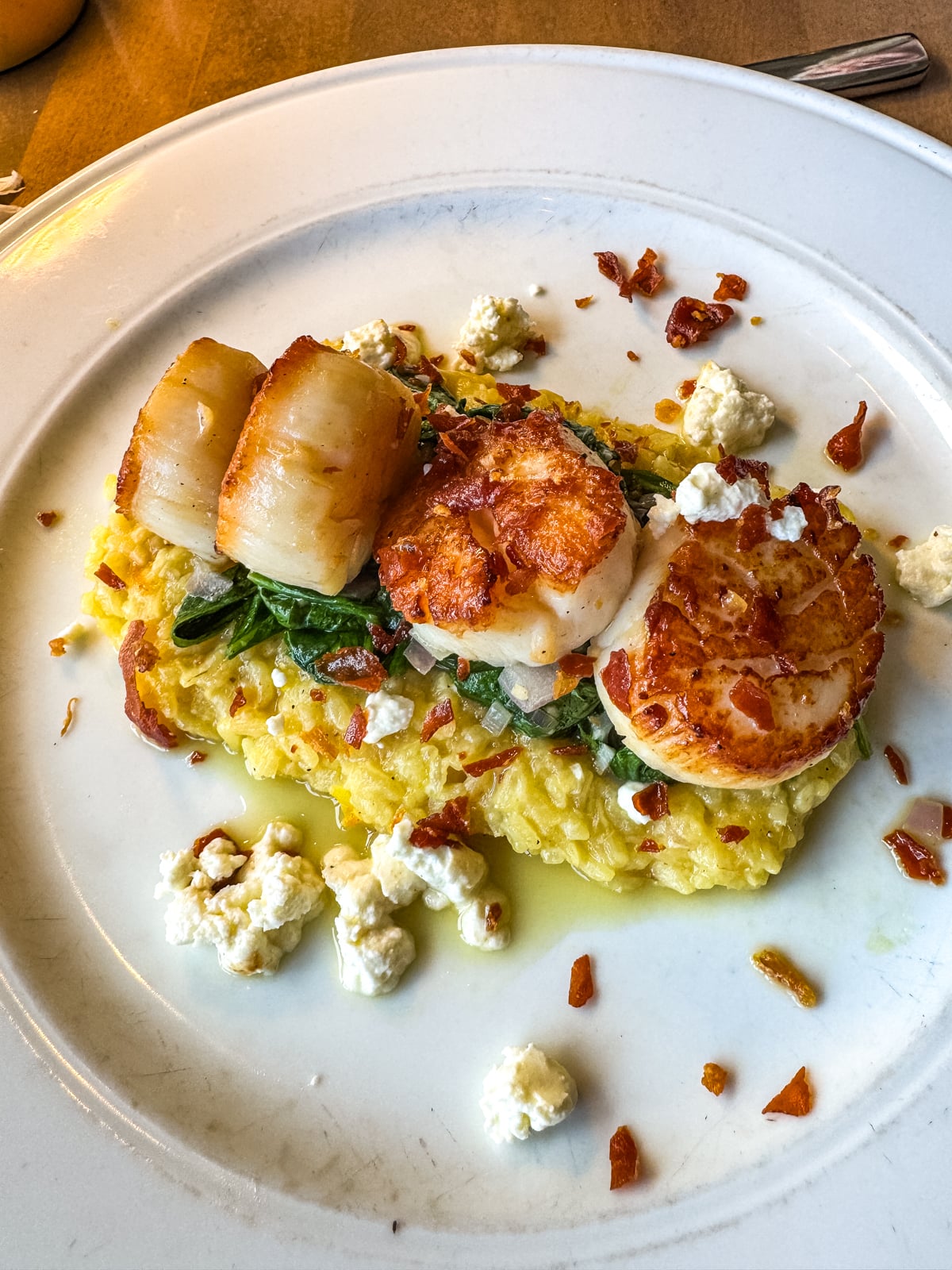Three seared scallops served on a bed of risotto with wilted greens, garnished with crumbled cheese and crispy bits&mdash;a must-try dish for your list of Things to Do in Roanoke VA.